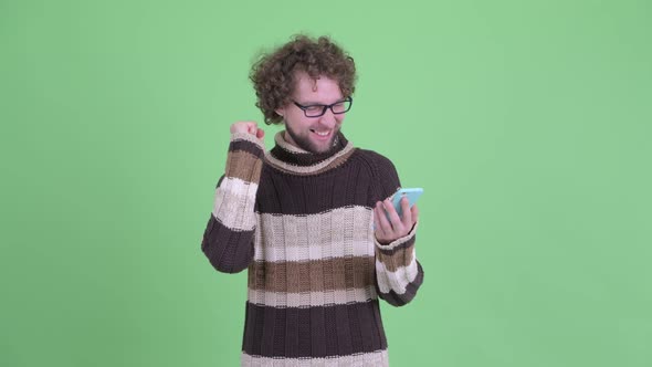 Happy Young Bearded Man Using Phone and Getting Good News