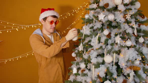 Man in Santa Hat and Fashionable Glasses Decorating Christmas Tree at Home