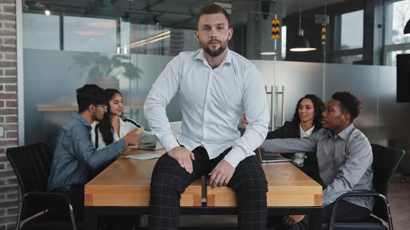Caucasian Pensive Young Male Leader Sitting on Table in Conference Room Confident Boss Smiling