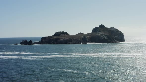 Majestic aerial drone footage, slowly tracking toward a very large Pacific ocean boulder which is su