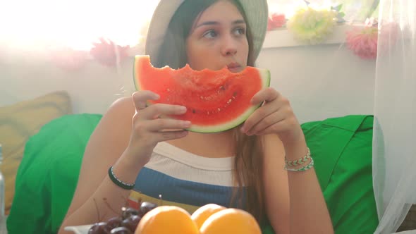 Young woman eating fresh watermelon in backyard tent