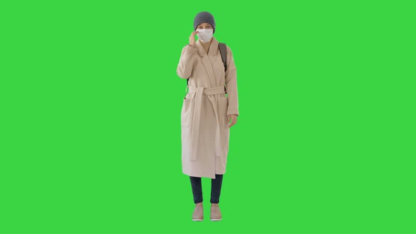 Girl in a Medical Face Mask Standing in a Coat on a Green Screen, Chroma Key