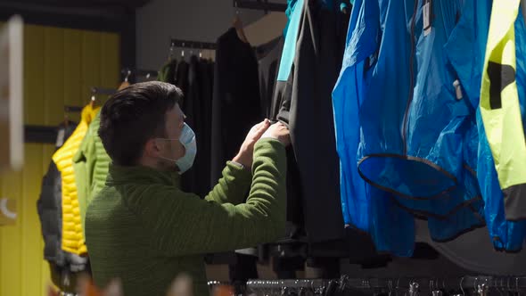 Masked Man in Sports and Outdoor Equipment Store Selects Jacket During Covid 19 Quarantine and Keeps