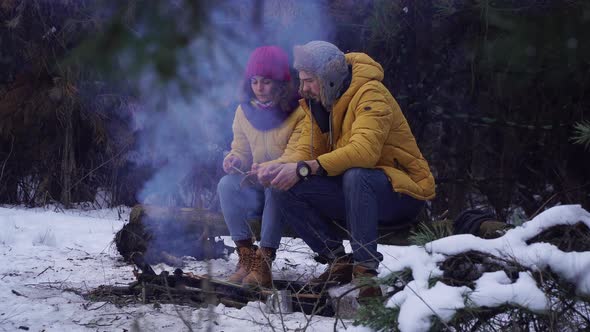 Young Man and Woman Near a Campfire in the Forest in Winter