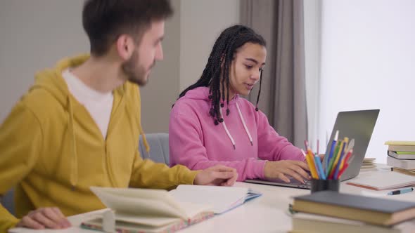 Side View of Confident Charming African American Girl Typing on Laptop Keyboard As Her Male