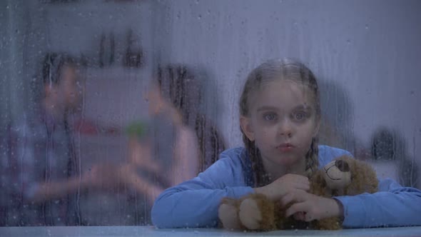 Girl Hugging Teddy Bear on Rainy Day, Father Choking Mother on Background