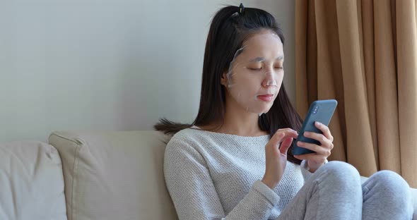 Woman apply paper mask on face at home with use of mobile phone