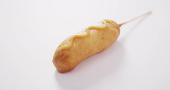 Video of corn dog with mustard on a white surface