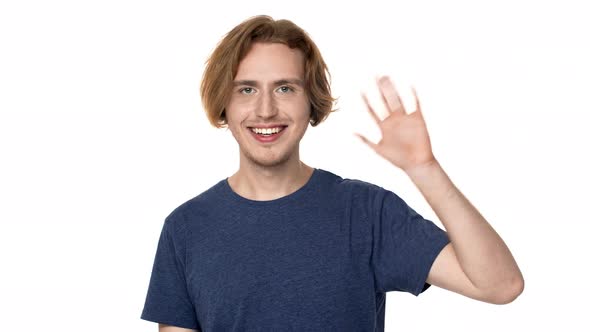 Portrait of Caucasian Young Guy in Casual Tshirt Smiling and Greeting or Welcoming with Waving Hand