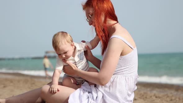 Happy Mother with Her Little Son Sitting on the Beach