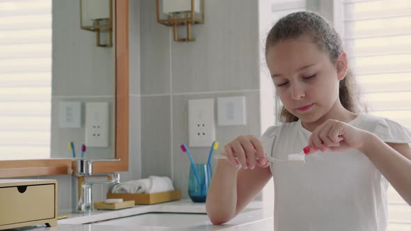 Portrait Happy Cute Young Teenage Girl Squeezing Toothpaste Onto Toothbrush in Her Bathroom