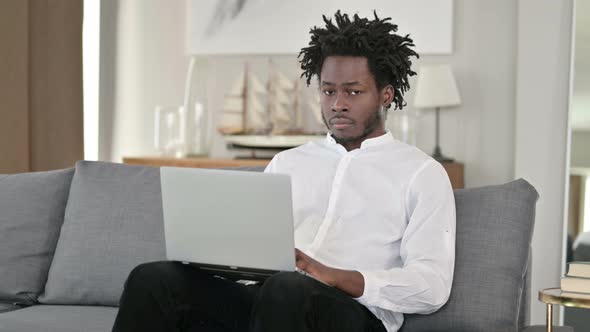 African Man with Laptop at Home Looking at Camera 