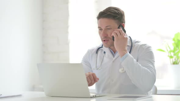 Male Doctor with Laptop Talking on Phone