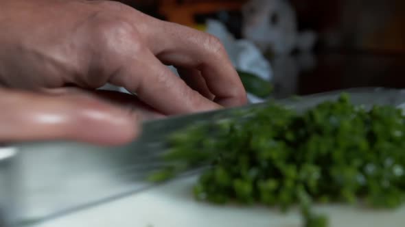 Close Up View of Knife Cutting Multiple Chives Into Pile of Small Vegetable Pieces