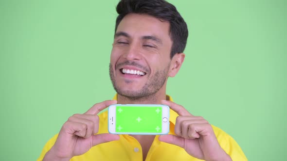 Face of Happy Young Hispanic Businessman Thinking While Showing Phone