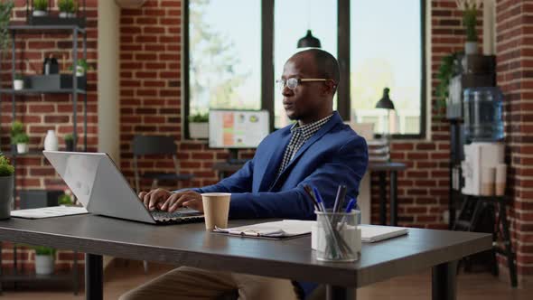 African American Worker Typing Email Report on Laptop