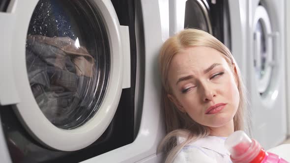 Closeup of a Young Woman with a Sad Expression Sitting By the Washing Machine in a Public Laundry