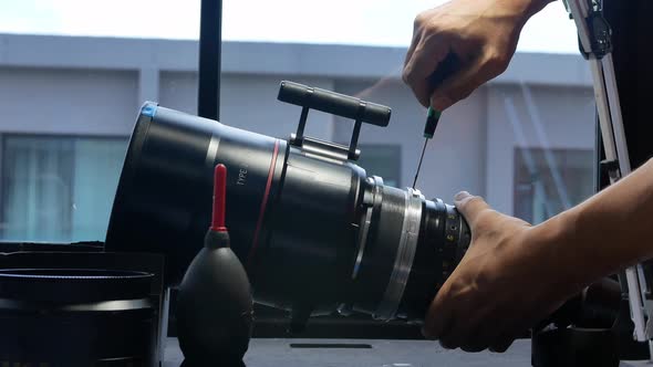 Using a screwdriver to remove screws on the barrel of a big movie camera zoom lens