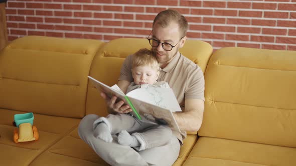 Father Reading Book Aloud to Cute Son at Home