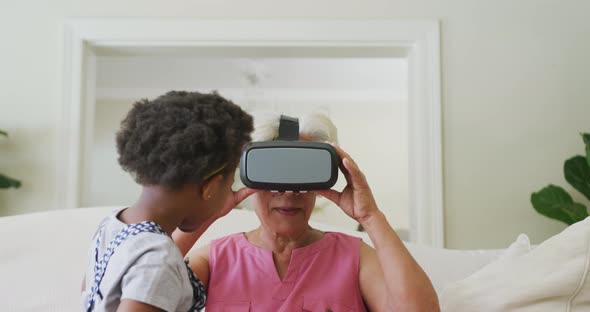 Happy african american grandmother using vr headset with granddaughter in living room