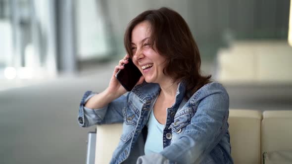 Cheerful Woman Is Talking By Cell Phone in Terminal of Airport, Waiting Flight, Lounge Area