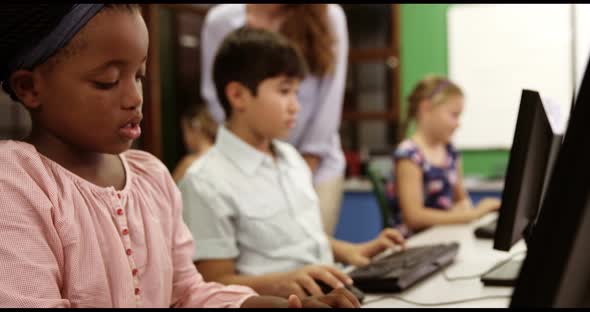 Teacher assisting school kids on personal computer in classroom