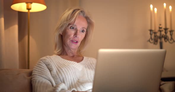 Portrait of Smiling Mature Woman Sitting on Couch Using Laptop and Having Virtual Conference