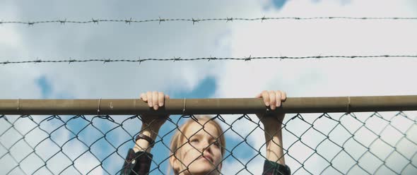 Young woman climbs metal fence and she is looking around over the fence