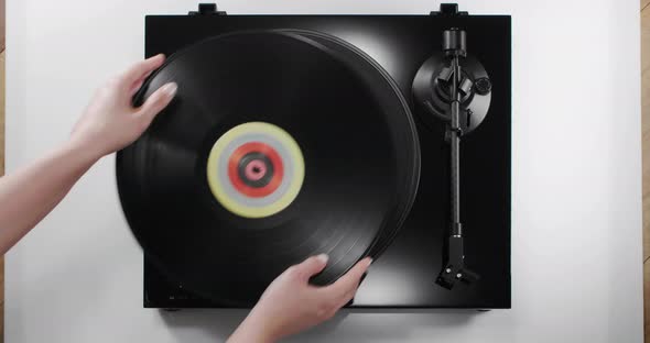 Hands Putting Vinyl Record on Black Turntable Top View