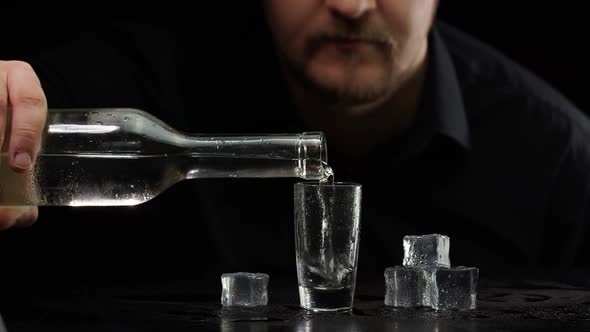 Bartender Pouring Up Frozen Vodka From Bottle Into Shot Glass with Ice Cubes on Black Background