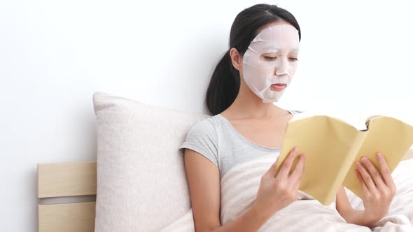 Woman use of paper mask on face and read book on bed 