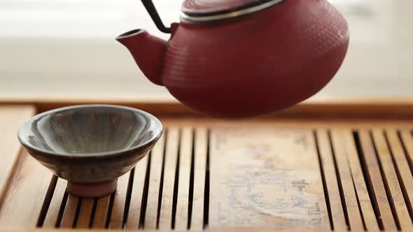 Tea is Poured Into a Bowl From a Red Chinese Teapot