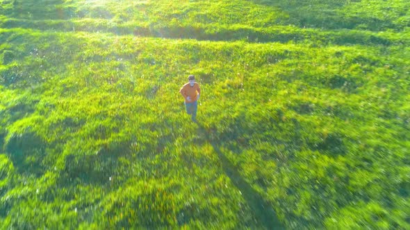 Flight Over Sporty Man Running at Perfect Green Grass Rural Meadow Offroad. Sunset in Mountain