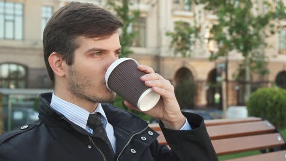 A Young Man Sits on a Bench and Drinks Coffee