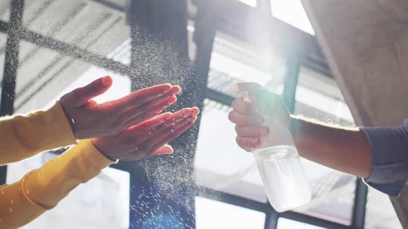 Mixed race male cafe worker wearing face mask disinfecting hands of female coworker