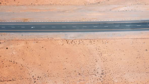 Tar road with cars through desert landscape, panning drone shot lef to right