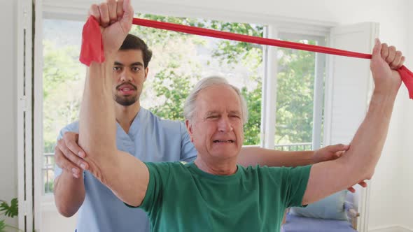 Biracial male physiotherapist with caucasian senior man holding resistance band while exercising