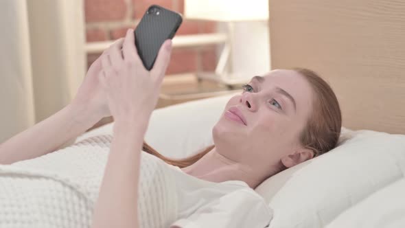 Handsome Redhead Young Woman Using Smartphone in Bed 