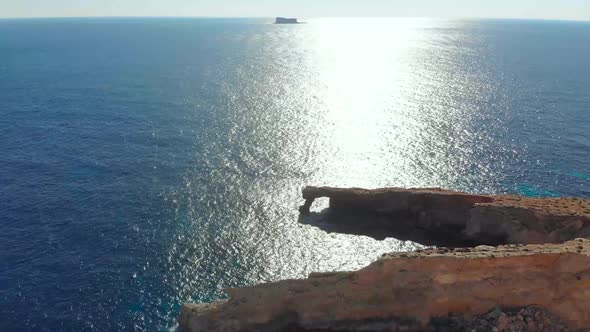 Drone shot over rocks in nature and towards a natural stone window on the Mediterranean sea of Malta