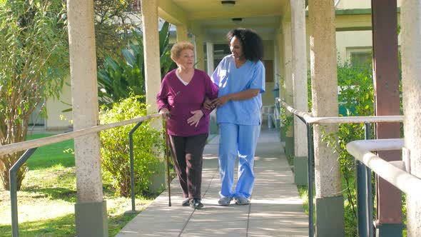 African Doctor Helps Elderly Woman with Walker in the Hospital Garden Patio  Slow Motion