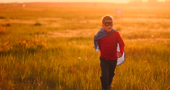 A Boy in a Suit and a Superhero Mask Running Across the Field at Sunset on the Grass