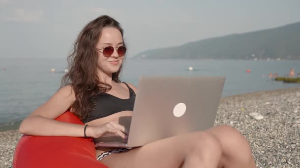 Successful Business Woman in Sunglasses Working on Laptop By the Sea at Public Beach