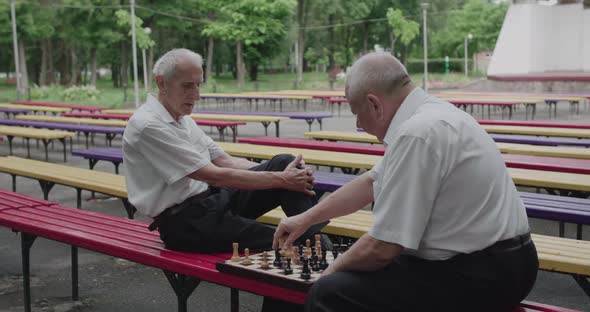 View of Chess Game Between Elder Thoughtful Men Having Relax on Outdoors Bench