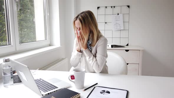 Sick businesswoman blowing nose while working in office