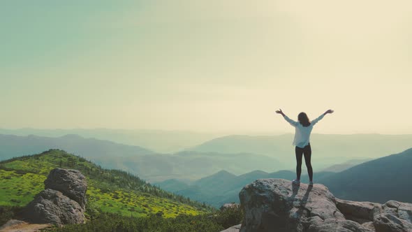 Woman Tourist Stands on a Rock with Arms Raised