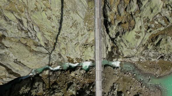 Aerial top down shot of high bridge between mountains and river on ground