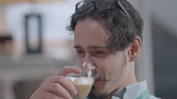 Headshot Portrait of Young Handsome Brunette Caucasian Man with Brown Eyes and Mustache Drinking