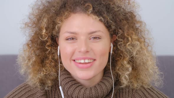 Video portrait of cheerful curly female in headset talking on camera with toothy smile in 4k video
