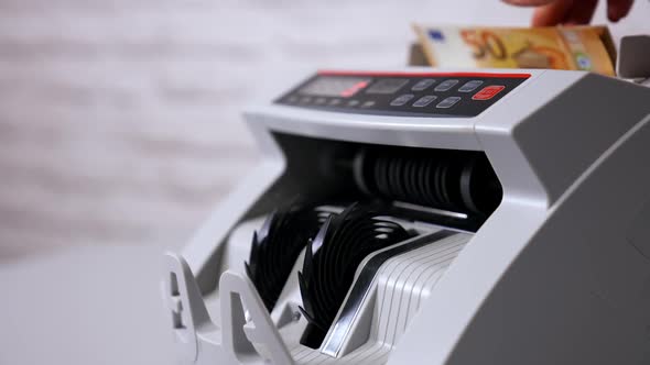 Female teller putting money into currency counting machine at cash department, close up