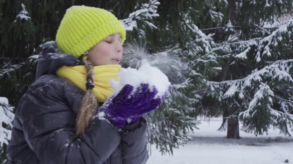 A Joyful Teenage Girl Blows on the Snow Having Fun in a Winter Park